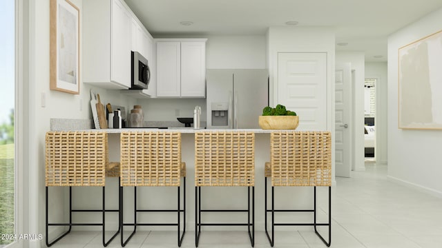 kitchen with white cabinets, light tile patterned floors, refrigerator with ice dispenser, and a kitchen breakfast bar