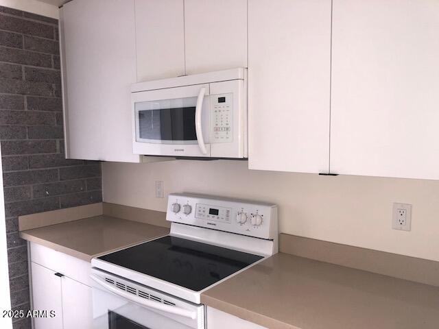 kitchen with white cabinetry, decorative backsplash, white appliances, and light countertops