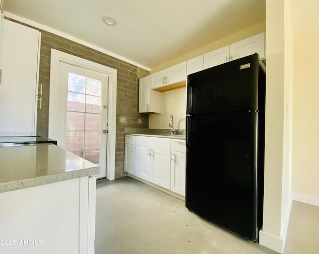kitchen featuring freestanding refrigerator, finished concrete flooring, white cabinetry, and a sink
