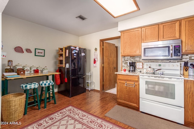 kitchen featuring tasteful backsplash, light wood-type flooring, electric stove, and black fridge