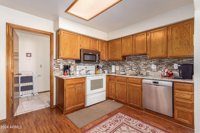 kitchen with dark tile floors, light stone countertops, backsplash, stainless steel appliances, and sink