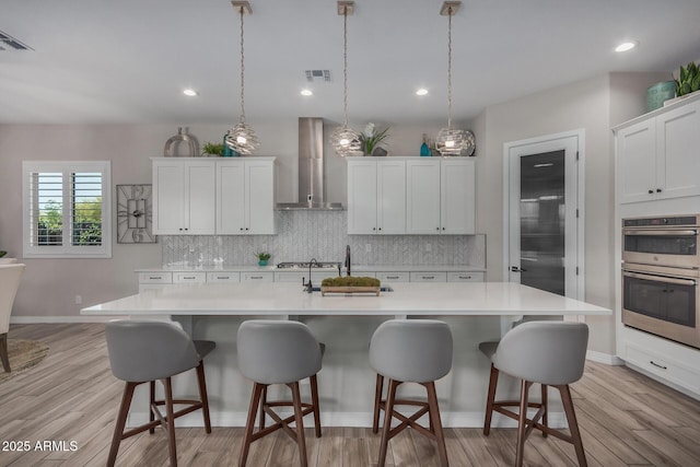 14571 W Wethersfield Rd, Surprise, AZ 85379 - kitchen with wall chimney exhaust hood, stainless steel double oven, light countertops, tasteful backsplash, and a center island with sink