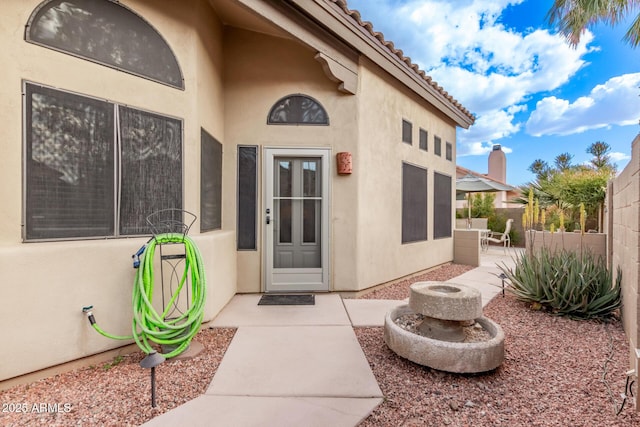 view of exterior entry featuring stucco siding, a patio area, and fence