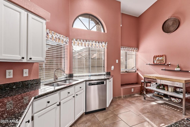 kitchen featuring stainless steel dishwasher, a sink, white cabinetry, dark stone countertops, and a high ceiling