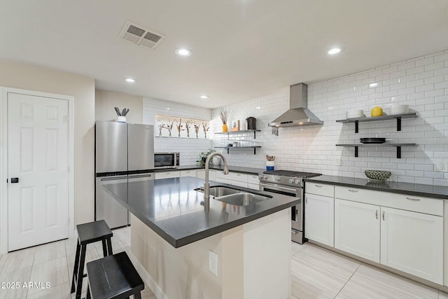 kitchen with a kitchen island with sink, wall chimney range hood, sink, white cabinetry, and stainless steel appliances