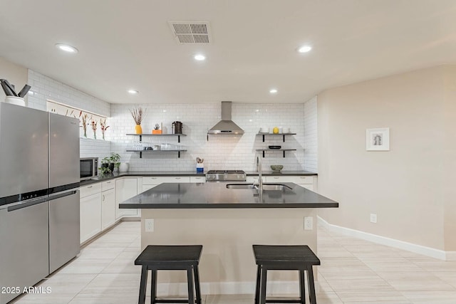 kitchen with a kitchen bar, white cabinets, stainless steel appliances, and wall chimney range hood