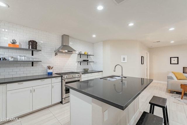 kitchen featuring tasteful backsplash, high end stainless steel range oven, sink, wall chimney range hood, and white cabinetry