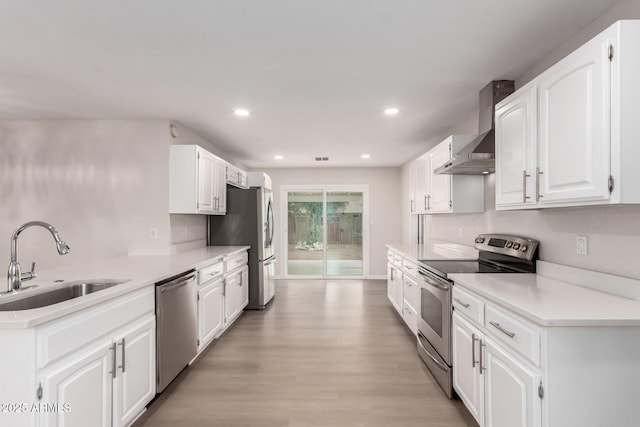 kitchen featuring a sink, stainless steel appliances, wall chimney exhaust hood, white cabinets, and light wood finished floors