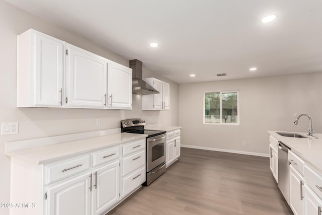 kitchen featuring light wood finished floors, a sink, stainless steel appliances, white cabinets, and wall chimney exhaust hood