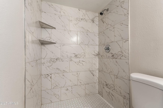 bathroom with a tile shower, toilet, and a textured wall