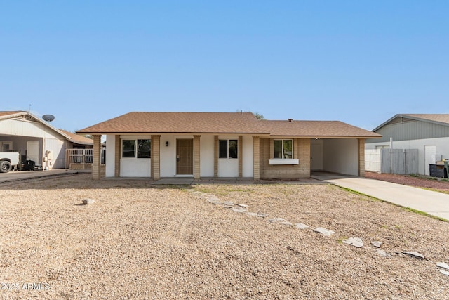 ranch-style house with a carport, fence, concrete driveway, a shingled roof, and brick siding