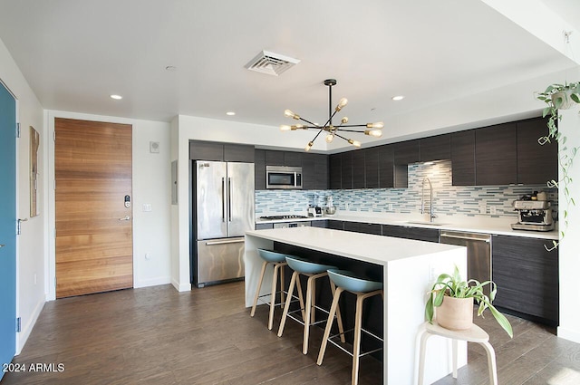 kitchen with appliances with stainless steel finishes, hardwood / wood-style flooring, sink, a kitchen island, and a breakfast bar