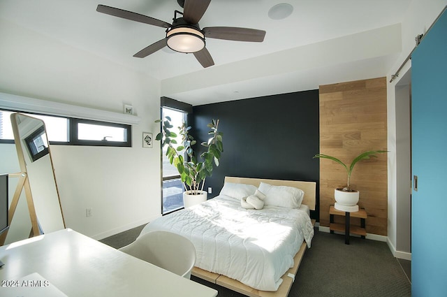 bedroom with ceiling fan, dark carpet, and a barn door