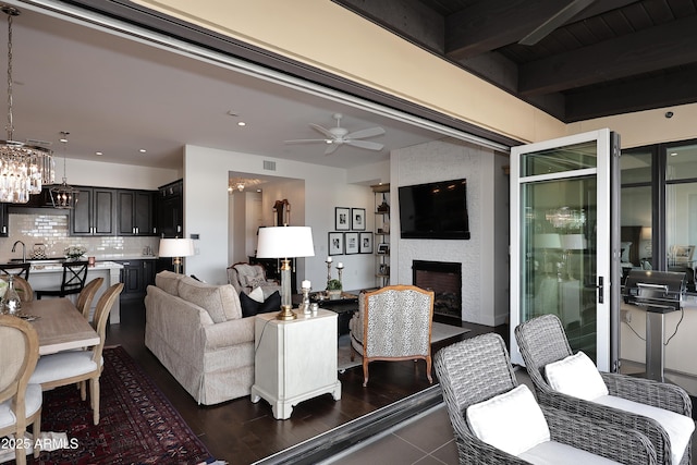 living area with visible vents, beam ceiling, recessed lighting, ceiling fan with notable chandelier, and a large fireplace