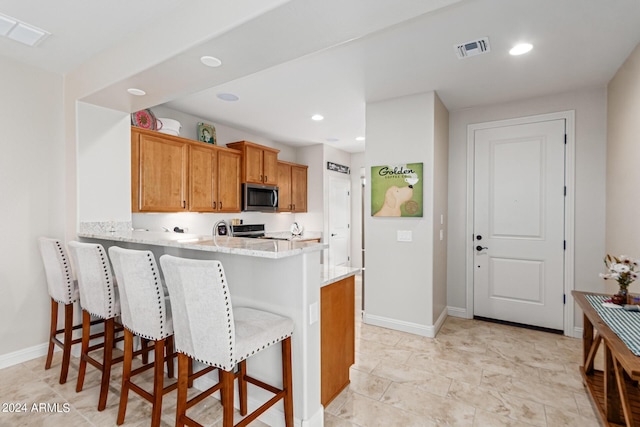 kitchen featuring kitchen peninsula, light stone countertops, a breakfast bar, and appliances with stainless steel finishes