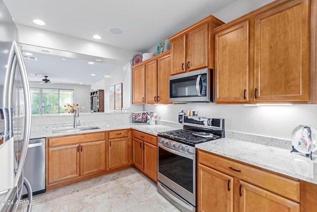 kitchen featuring light stone counters, sink, ceiling fan, and appliances with stainless steel finishes