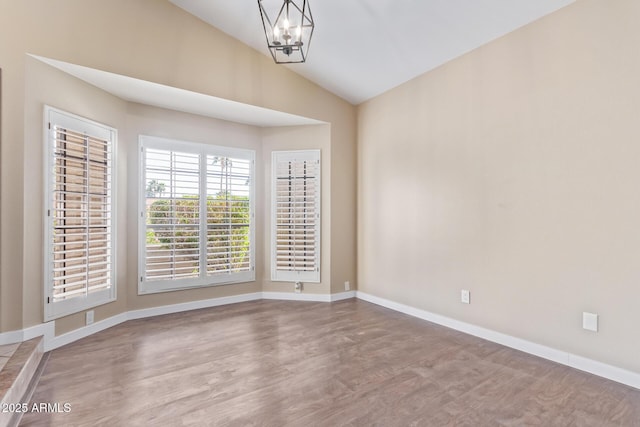 spare room with a notable chandelier, hardwood / wood-style flooring, and vaulted ceiling