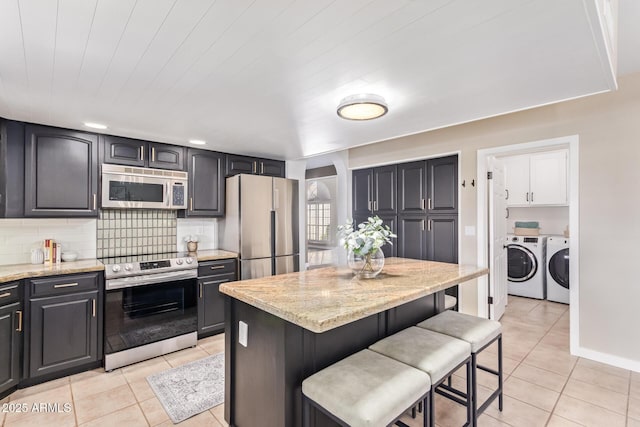 kitchen featuring stainless steel appliances, a kitchen island, washing machine and clothes dryer, and a kitchen bar