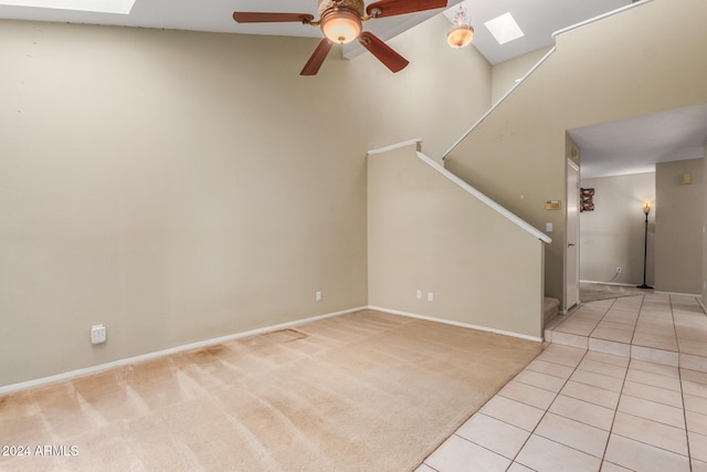 unfurnished living room with ceiling fan, high vaulted ceiling, a skylight, and light tile patterned floors