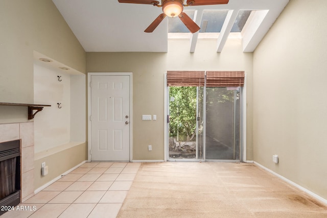 unfurnished living room with ceiling fan, vaulted ceiling with skylight, light tile patterned floors, and a tile fireplace