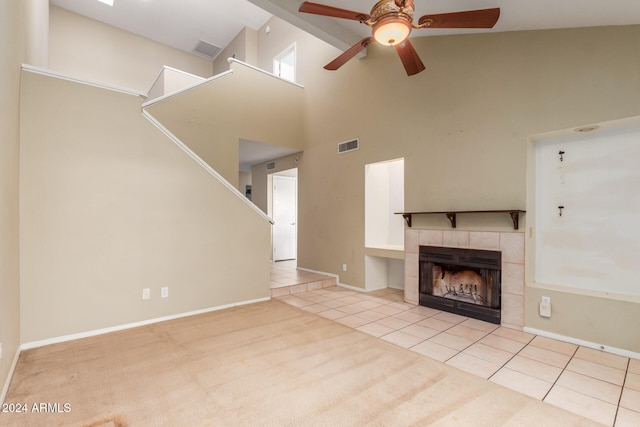 unfurnished living room featuring a tiled fireplace, high vaulted ceiling, light colored carpet, and ceiling fan