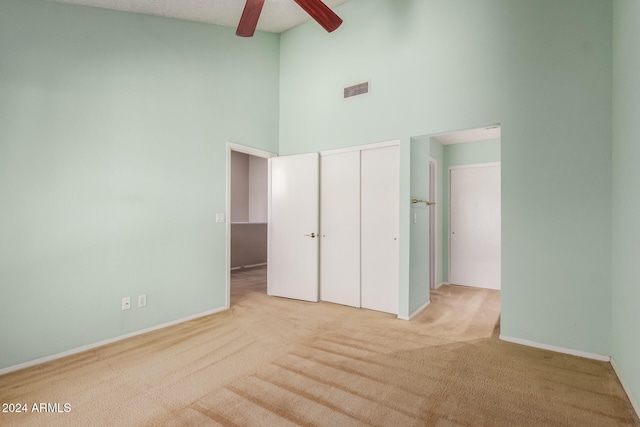 unfurnished bedroom featuring a closet, ceiling fan, high vaulted ceiling, and light carpet