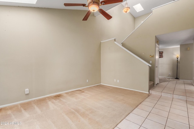 unfurnished living room with ceiling fan, a skylight, stairway, light carpet, and light tile patterned flooring