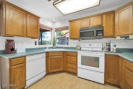 kitchen featuring brown cabinetry, white appliances, light wood-style floors, and a sink
