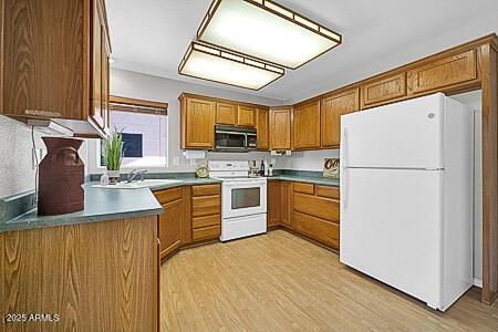 kitchen featuring white appliances, a sink, brown cabinetry, and light wood finished floors