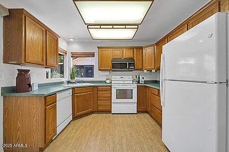 kitchen featuring brown cabinetry, light wood-style flooring, and white appliances