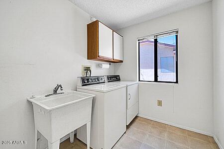 laundry room with baseboards, a sink, a textured ceiling, cabinet space, and washing machine and dryer