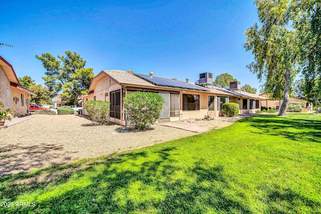 rear view of house featuring central air condition unit, a yard, and solar panels