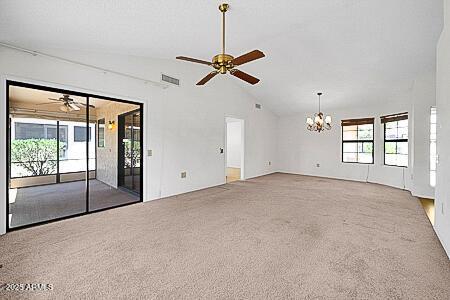 unfurnished living room featuring ceiling fan with notable chandelier, visible vents, lofted ceiling, and carpet
