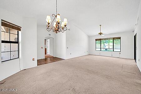 spare room featuring arched walkways, ceiling fan with notable chandelier, lofted ceiling, and carpet