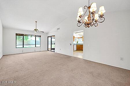 unfurnished living room featuring high vaulted ceiling, carpet flooring, and ceiling fan with notable chandelier