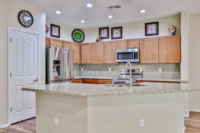 kitchen with visible vents, a kitchen island with sink, light wood-style floors, appliances with stainless steel finishes, and decorative backsplash