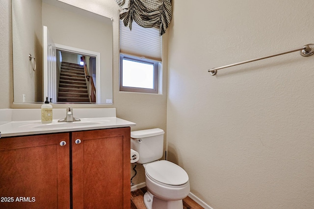 half bath with baseboards, toilet, wood finished floors, and vanity