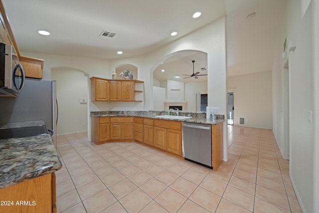 kitchen with appliances with stainless steel finishes, sink, dark stone countertops, light tile patterned floors, and ceiling fan