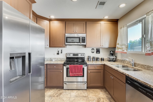 kitchen with appliances with stainless steel finishes, light tile patterned floors, light stone counters, and sink