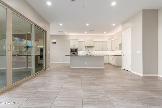 kitchen with tasteful backsplash, white cabinetry, sink, stainless steel microwave, and a kitchen island with sink