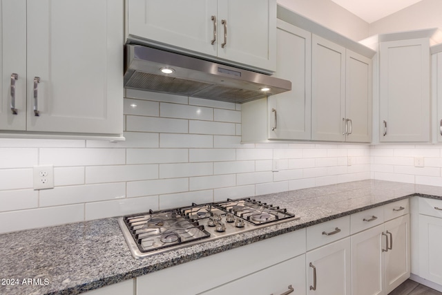 kitchen featuring white cabinets, stainless steel gas cooktop, dark stone countertops, and tasteful backsplash