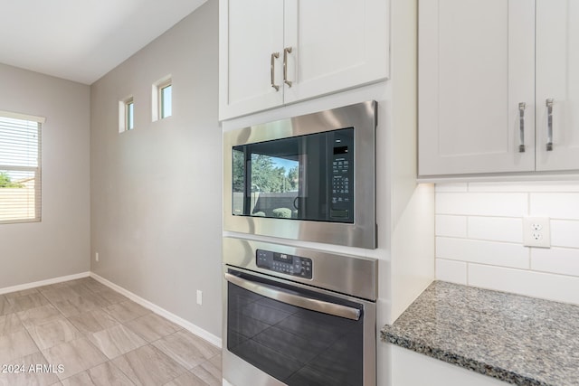 kitchen featuring stainless steel appliances, white cabinets, decorative backsplash, and dark stone counters