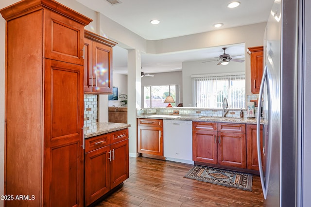 kitchen featuring dishwasher, backsplash, dark wood-type flooring, light stone countertops, and stainless steel refrigerator