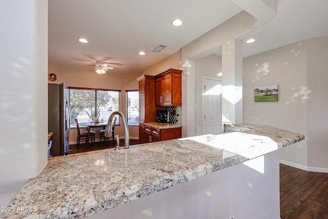 kitchen with kitchen peninsula, stainless steel fridge, tasteful backsplash, light stone counters, and dark hardwood / wood-style floors