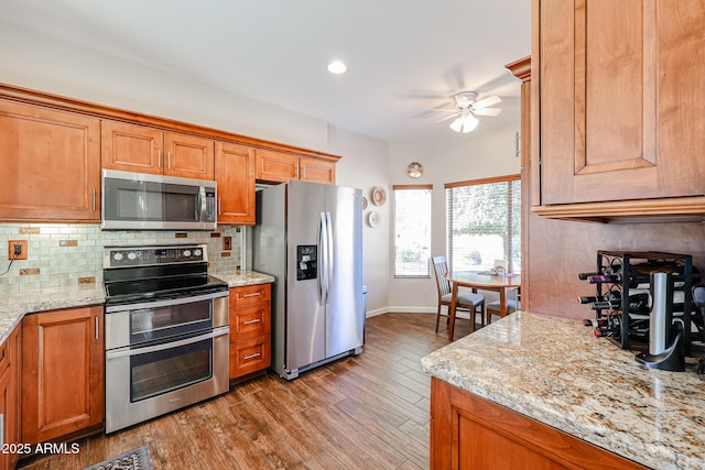 kitchen featuring light stone countertops, light wood-type flooring, appliances with stainless steel finishes, and backsplash