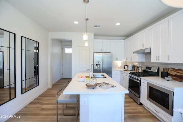 kitchen with under cabinet range hood, stainless steel appliances, visible vents, light countertops, and decorative backsplash