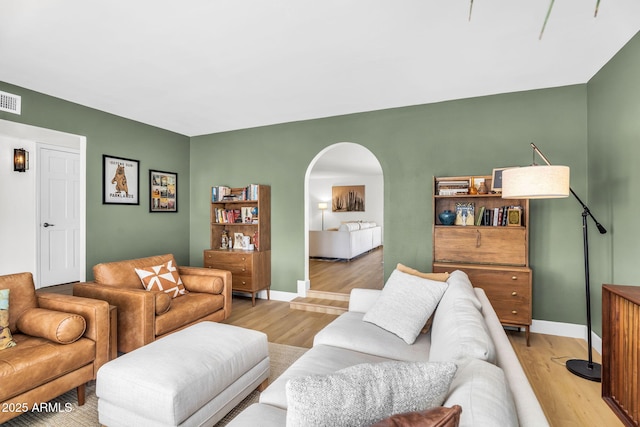 living area featuring arched walkways, visible vents, light wood-style flooring, and baseboards