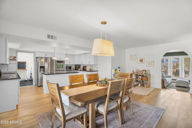 dining space featuring light wood-style flooring, arched walkways, and visible vents