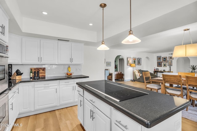 kitchen featuring visible vents, light wood-style flooring, dark countertops, arched walkways, and black electric cooktop