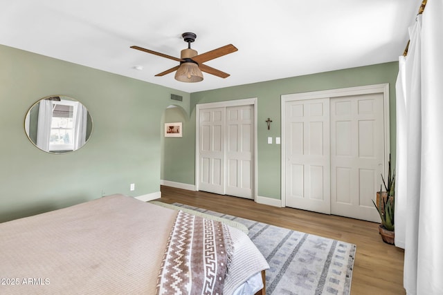 bedroom featuring wood finished floors, visible vents, baseboards, arched walkways, and multiple closets